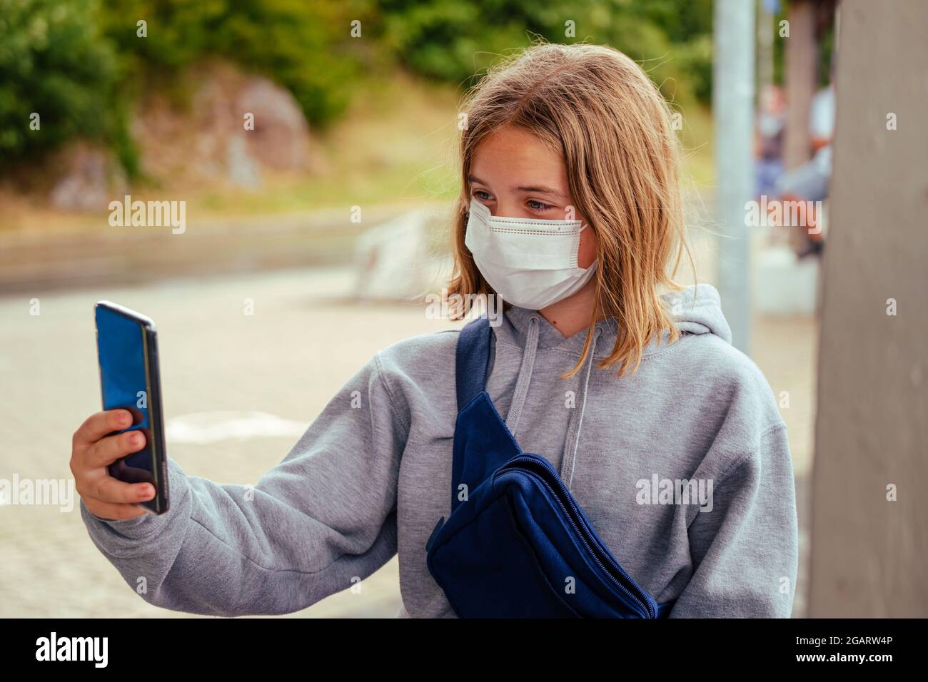 Portrait d'une jeune fille caucasienne de 12 ans portant un masque blanc et un sweat à capuche gris prenant un selfie à l'extérieur Banque D'Images