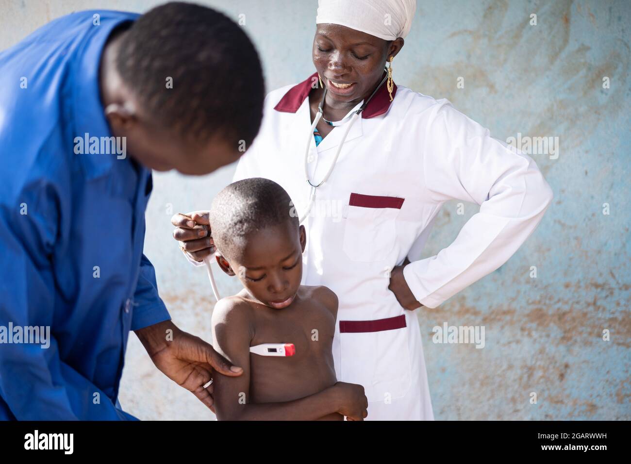 Dans cette image, une jeune infirmière noire parle à un petit garçon africain inquiet subissant un dépistage de température avec un thermomètre numérique au cours d'un routi Banque D'Images