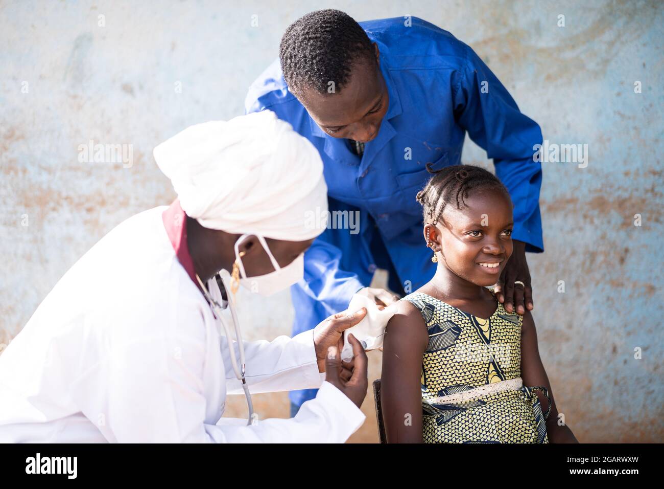 Dans cette image, une jeune fille africaine souriante se voit injecter une dose de vaccin dans la partie supérieure du bras par une pédiatre femelle noire avec masque et unifor blanc Banque D'Images
