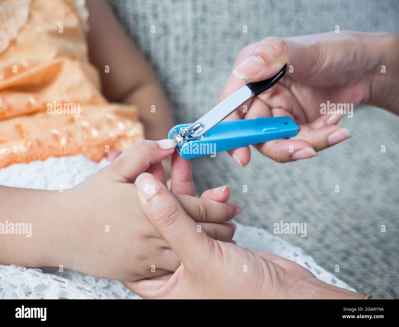 La mère coupe les ongles de la petite fille sur les doigts. Pédicure. Maternité. Soins. Ciseaux. Banque D'Images