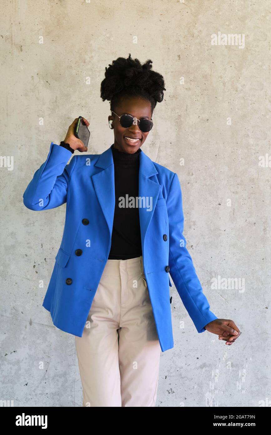 Femme africaine portant des écouteurs sans fil, dansant sur un mur de béton. Banque D'Images