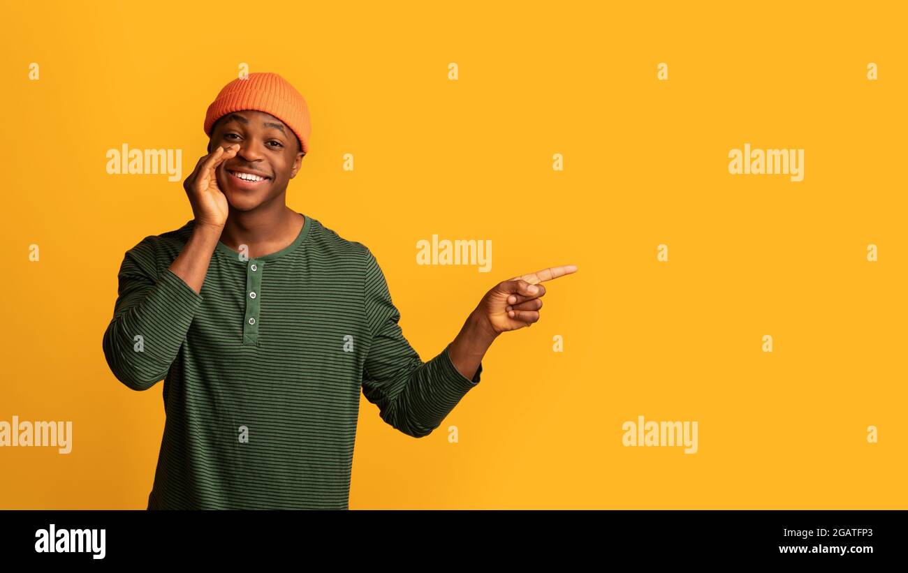 Regardez ceci. Happy Young African American Guy pointant de côté à Copy Space, gai Black Man gardant la main près de la bouche, recommandant Nice offre pendant Banque D'Images