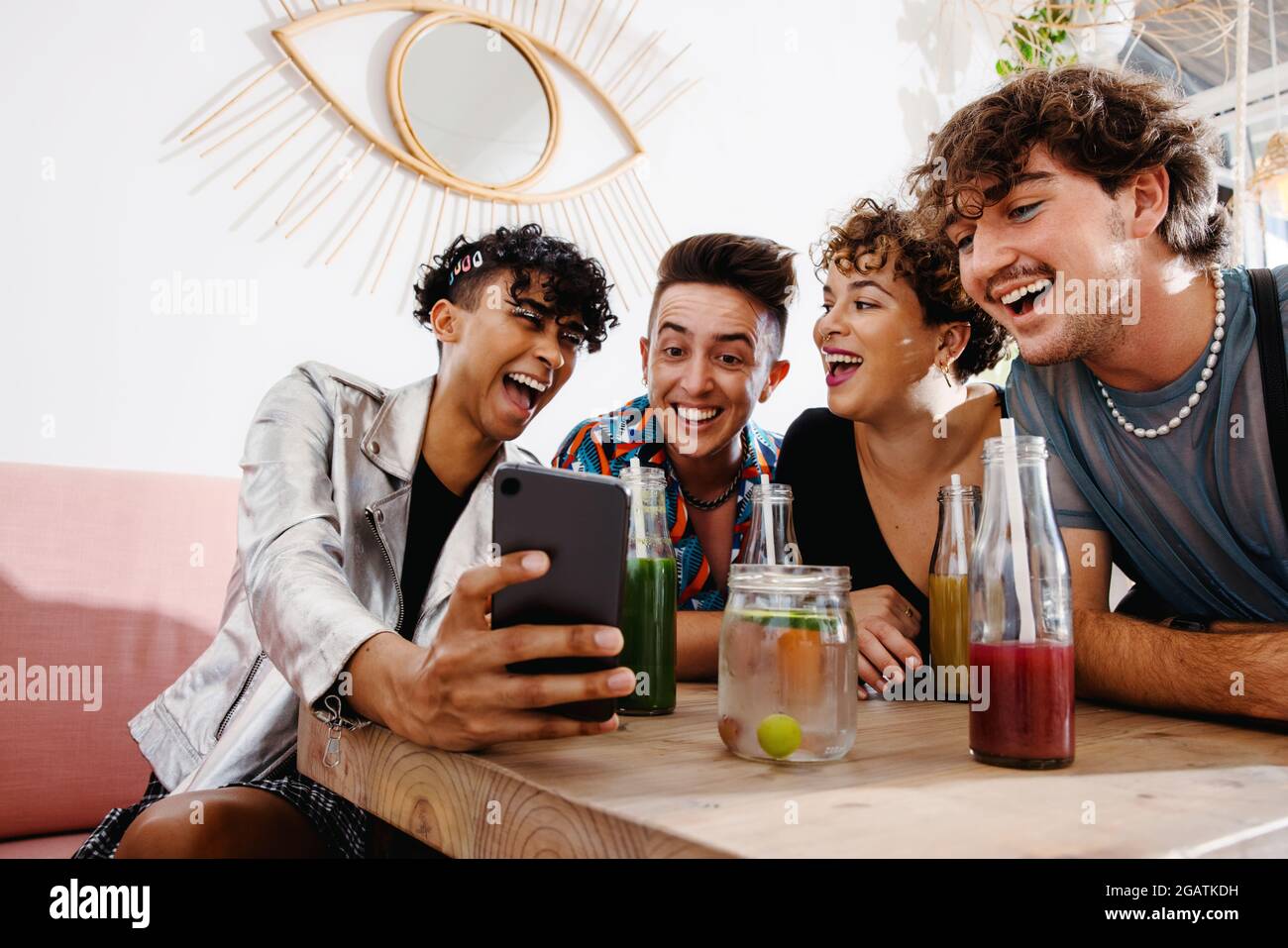 Groupe souriant d'amis en streaming en ligne tout en étant assis dans un restaurant. Groupe de quatre jeunes queer qui s'amusent ensemble pendant le déjeuner. Réfrigérateur Banque D'Images