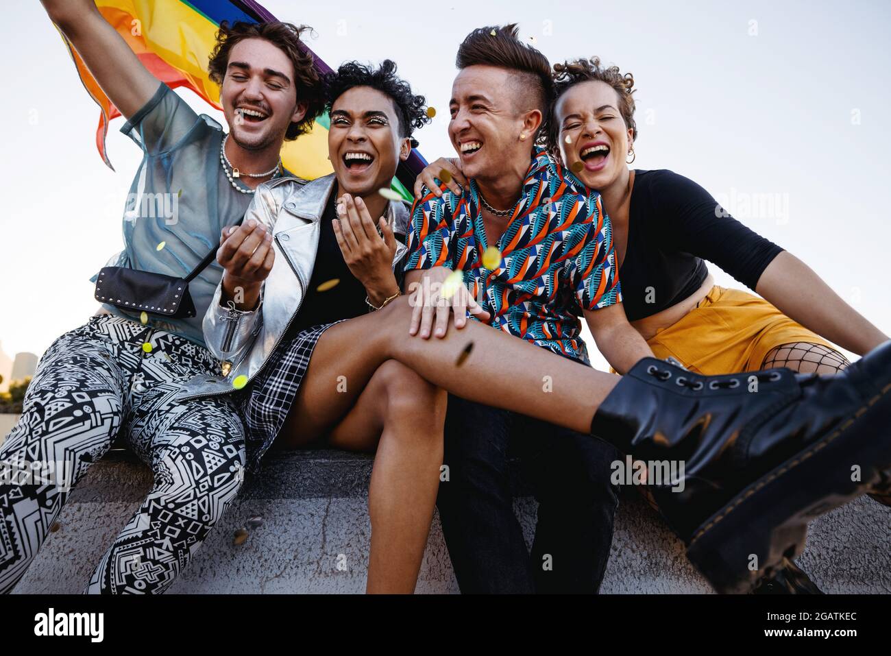 Les jeunes célèbrent leur fierté tout en étant assis ensemble. Quatre membres de la communauté LGBTQ+ sourient joyeusement tout en levant le drapeau de la fierté. Groupe de Banque D'Images