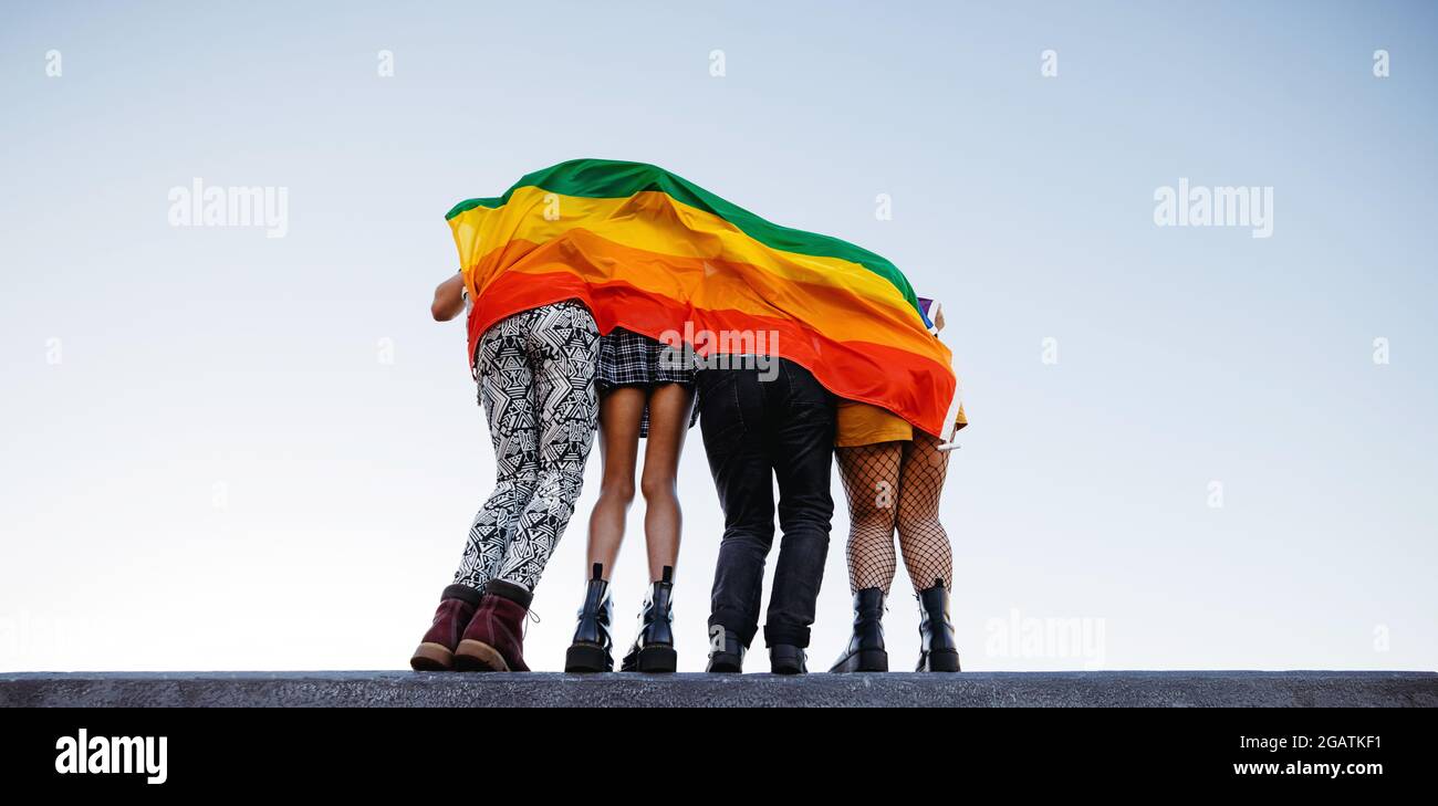 Groupe anonyme de personnes debout derrière un drapeau de fierté arc-en-ciel. Groupe d'individus queer qui embrassent leur identité. Quatre membres du LG Banque D'Images