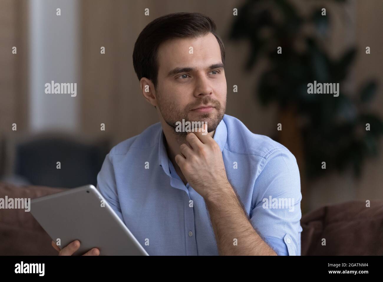 Un jeune homme d'affaires sérieux utilisant une tablette, en regardant de côté avoir l'idée Banque D'Images