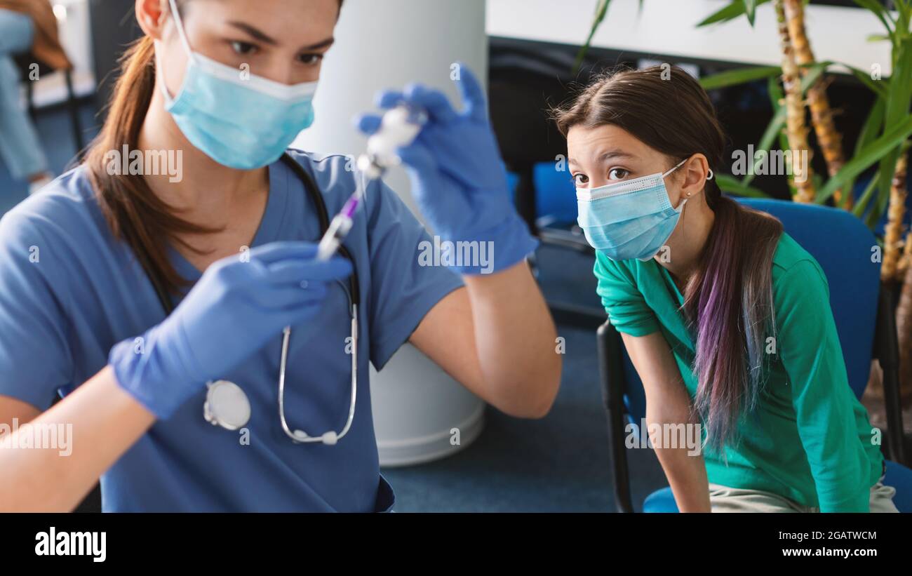 Concept de vaccination. Une infirmière de sexe féminin remplissant une seringue en tirant le médicament hors du flacon avant de lui donner un jab. Accent sélectif sur l'adolescence fille en attente de COV Banque D'Images