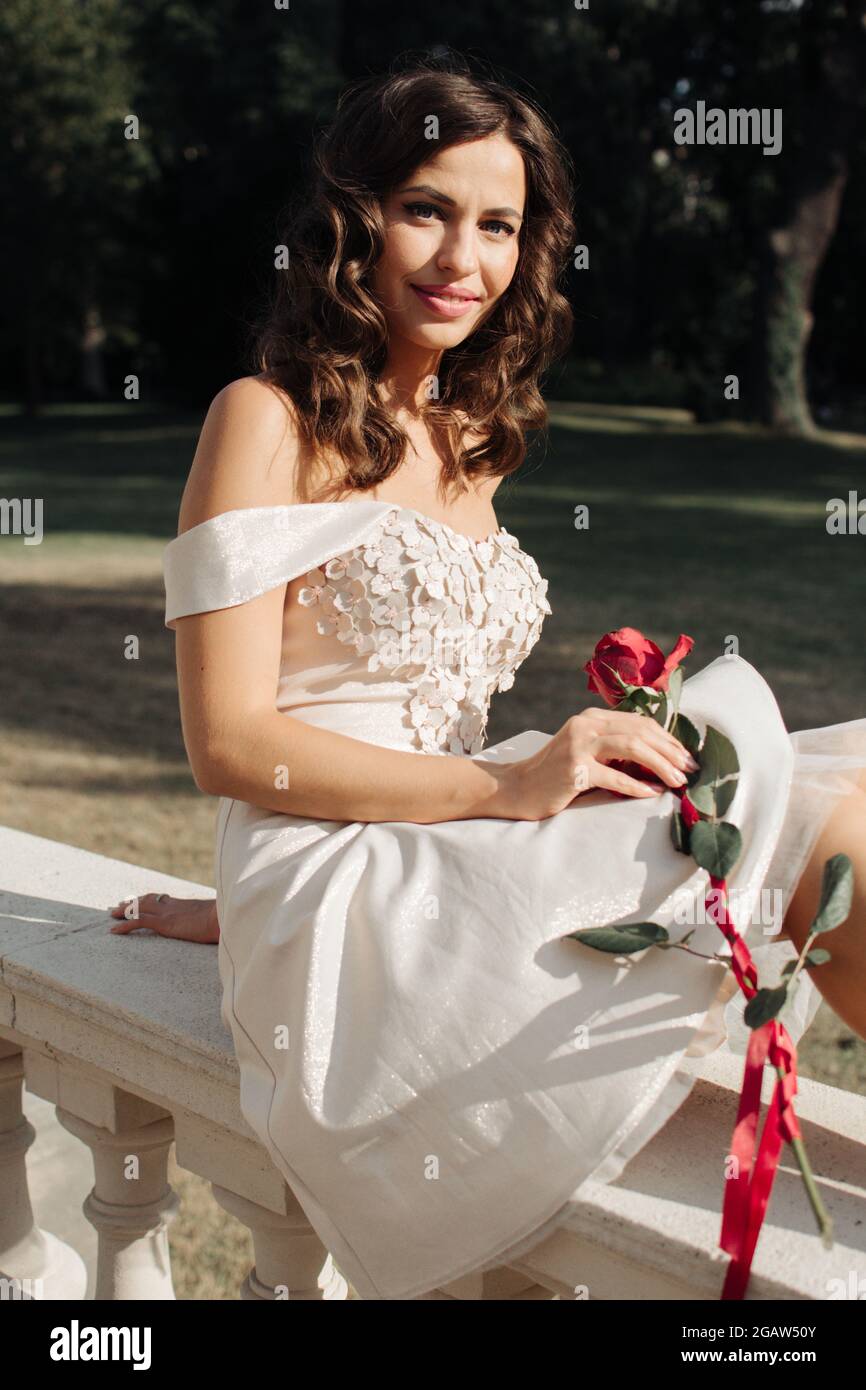 Jeune belle dame en robe blanche avec rose rouge se dresse à côté d'une  statue Photo Stock - Alamy