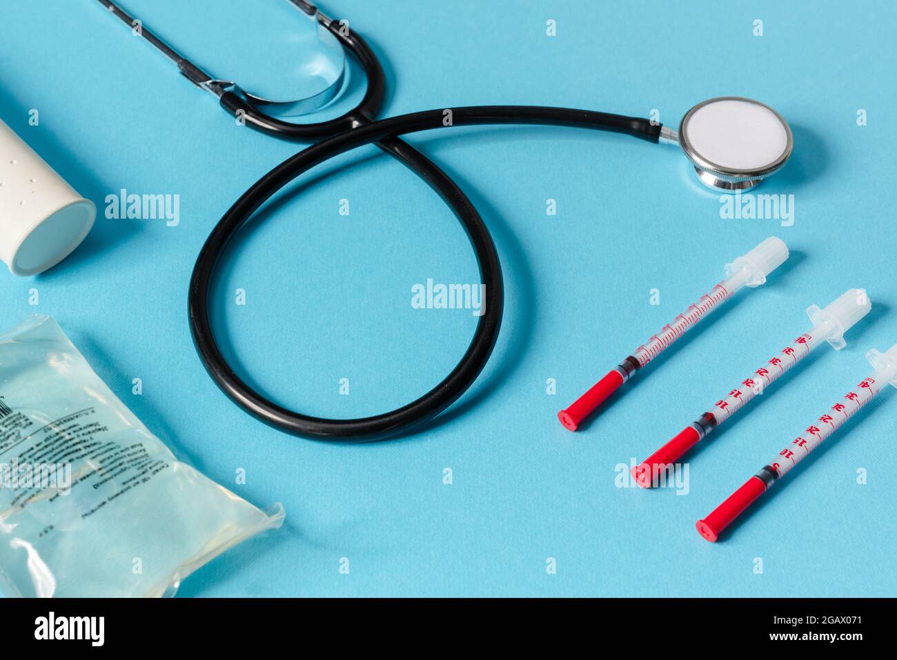 Vue rapprochée d'un instrument médical constitué d'un stéthoscope, de seringues, d'un contenant de liquide et d'un thermomètre reposant sur un fond bleu dans une unité de mesure de la température Banque D'Images