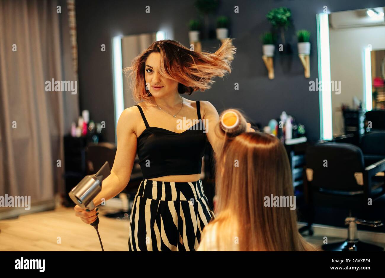 Une femme heureuse avec la styliste qui fait une coiffure au salon. Coiffeur féminin compétent décider quoi faire dans un salon de coiffure avec une cliente brune. Deux beaut Banque D'Images