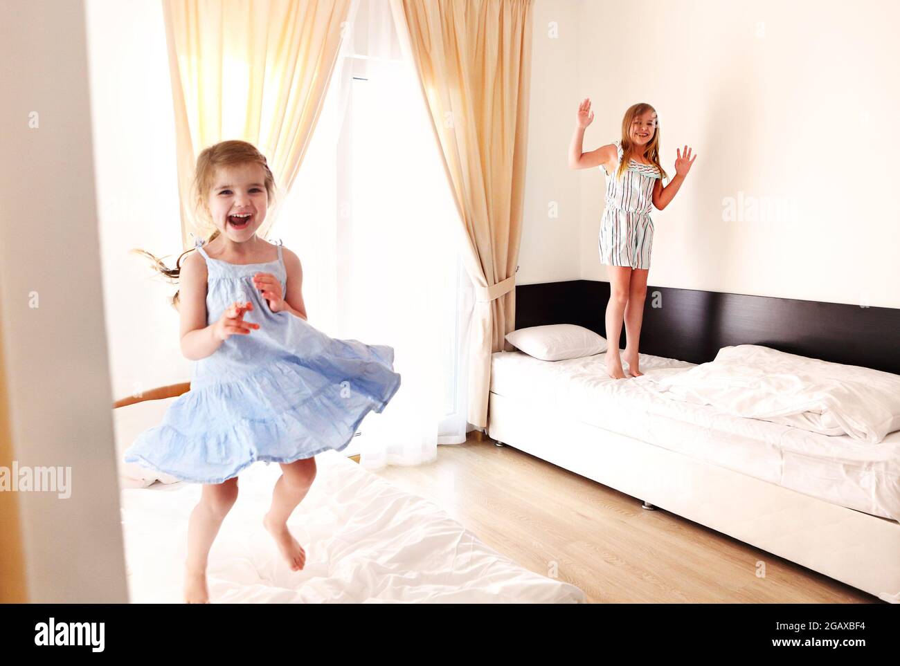 Deux petites sœurs mignonnes et insouciantes filles dans des vêtements décontractés jouant en s'amusant dans la chambre des enfants le matin ensoleillé. Les enfants aiment bondir sur les lits Banque D'Images