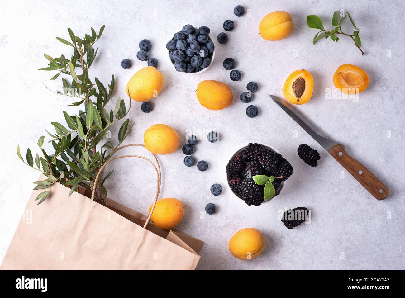 Achat de baies d'été, sac en papier et abricots, bleuets, mûres dispersées sur fond blanc, nourriture saine. Banque D'Images