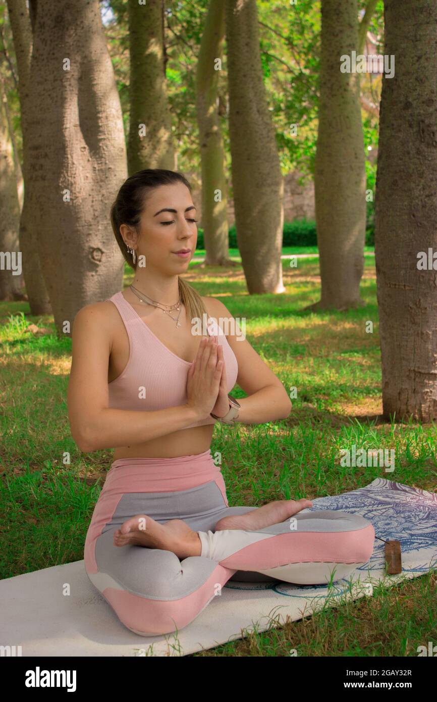 Image verticale jeune femme assise tapis de yoga appréciant l'exercice froid pilaté tenant les mains en position de prière après l'entraînement. Pilates extérieur 2021 Banque D'Images