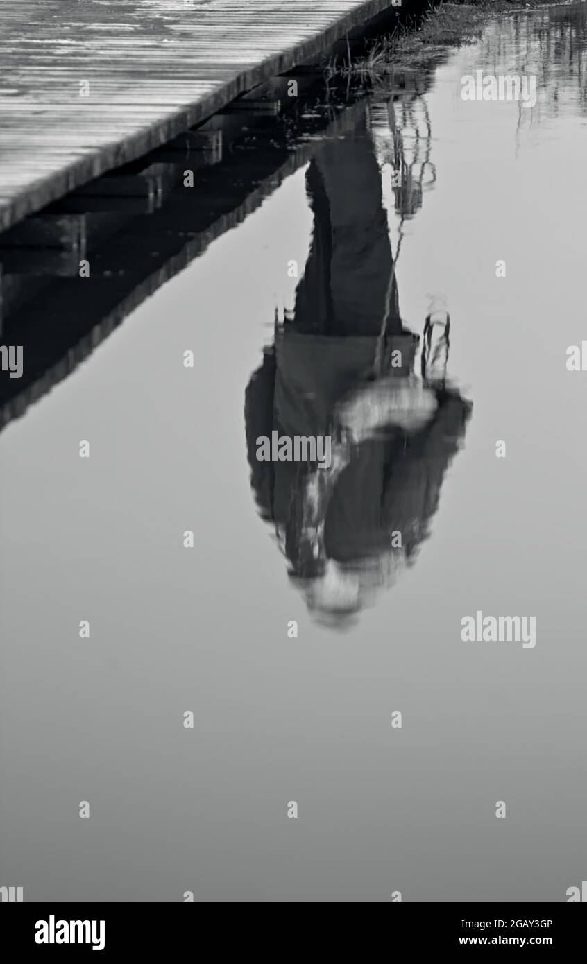 Réflexion d'UN homme portant UNE ceinture de sauvetage en bateau traversant un pont de promenade en bois réfléchi dans l'eau. Christchurch Royaume-Uni Banque D'Images