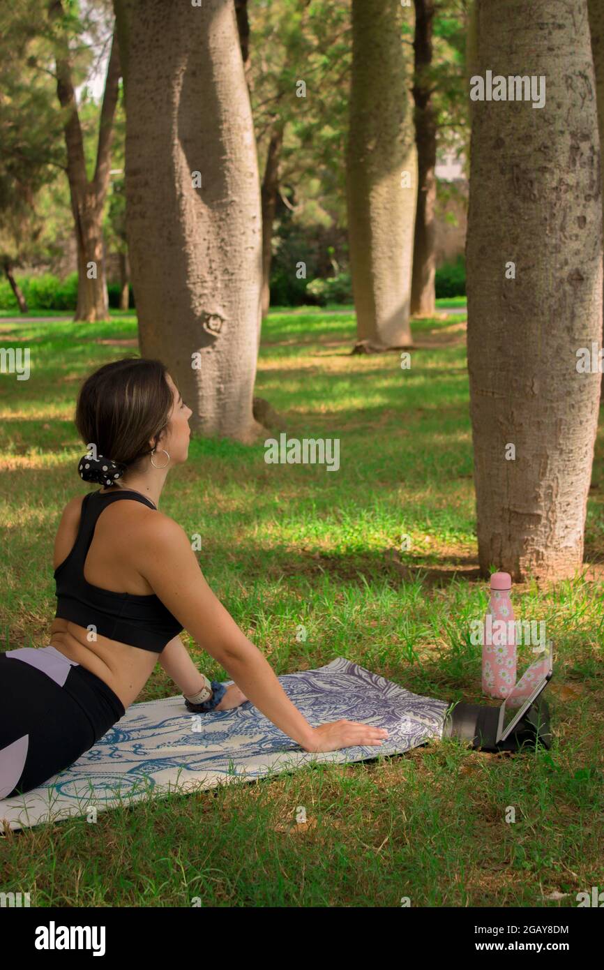 Image verticale d'une jeune fille qui fait la pose de cobra pendant qu'elle se détend à l'extérieur dans le parc de la ville dans un été ensoleillé jour. Pilates extérieur 2021. Banque D'Images