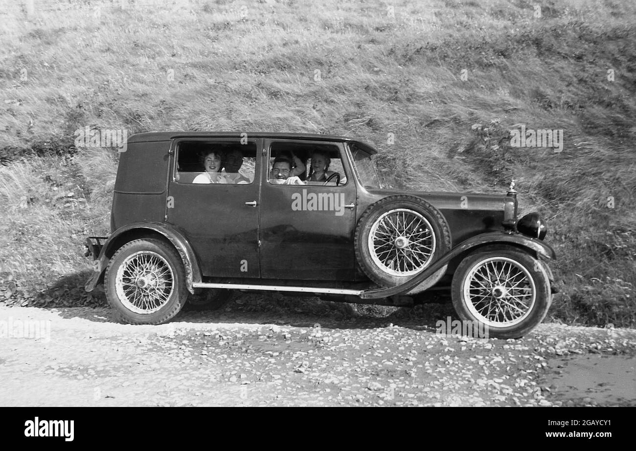 années 1930, historique, à l'extérieur sur une piste de gravier dans une zone touristique de campagne, une famille assise dans une voiture à quatre portes, à roues de l'époque, fenêtres vers le bas, regardant dehors, souriant. Banque D'Images