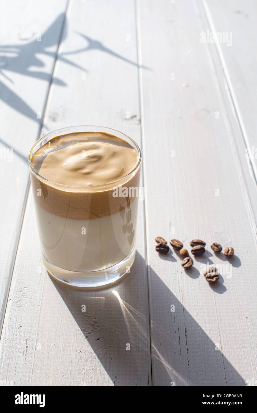 Boisson traditionnelle coréenne avec de la caféine, le café Dalgona dans un verre transparent avec des grains de café sur fond de tableaux blancs. Lait avec fouetté Banque D'Images
