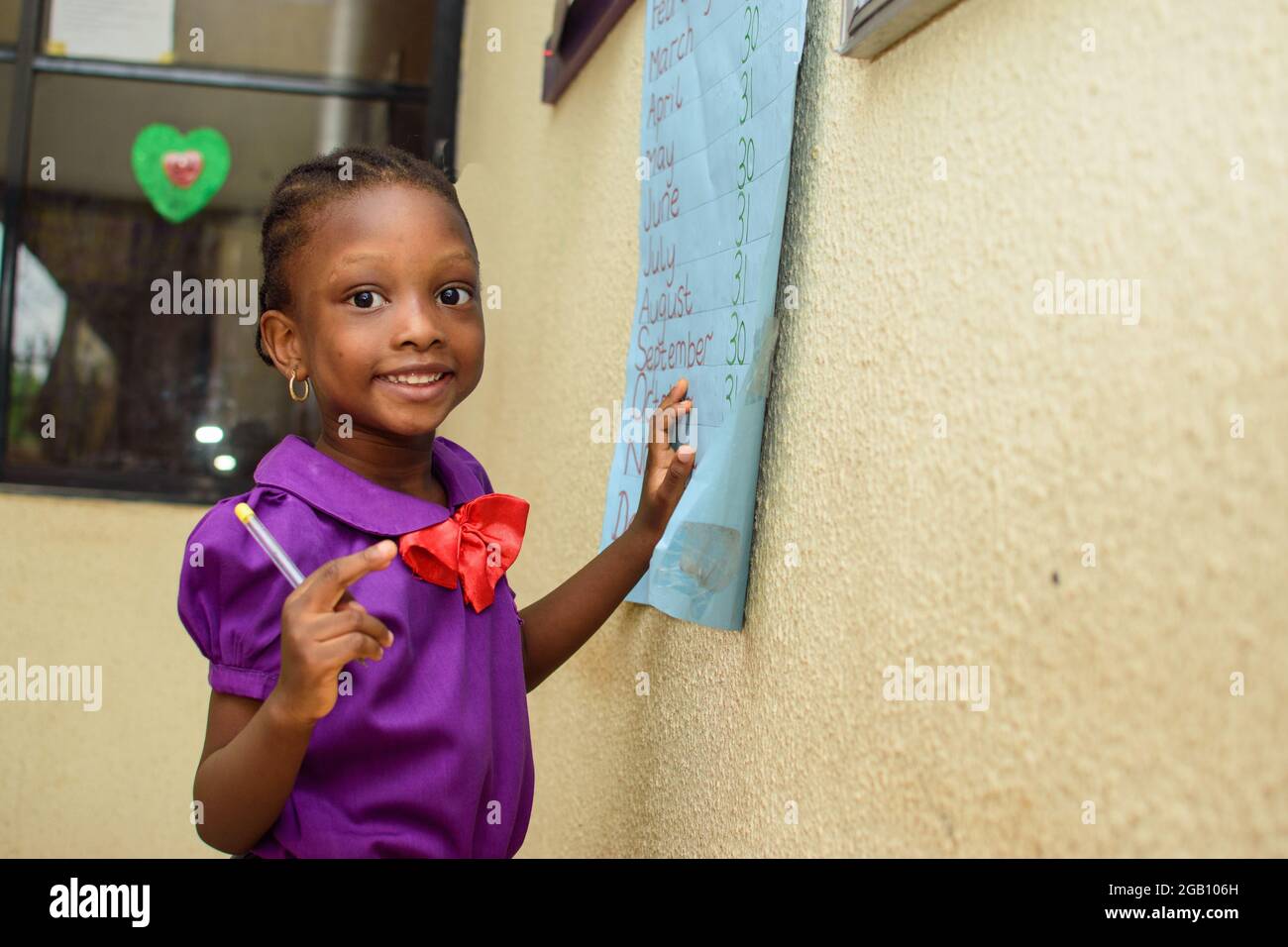 Fille africaine portant un uniforme scolaire violet et debout dans une  salle de classe avec un stylo à la main pour étudier pour l'excellence dans  son éducation Photo Stock - Alamy