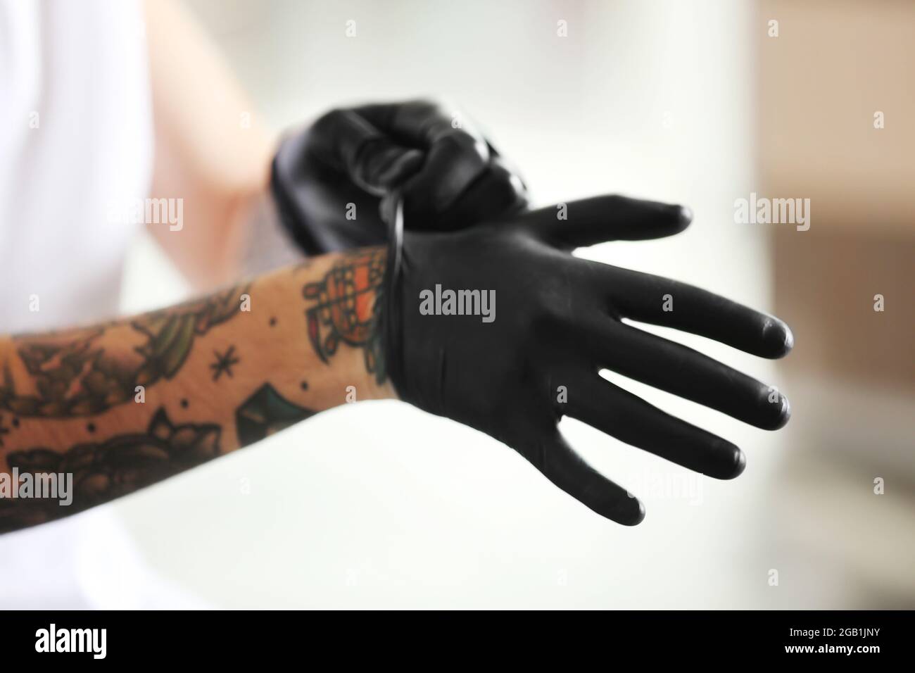 Homme avec tatouage portant des gants en latex noir sur fond flou Photo  Stock - Alamy