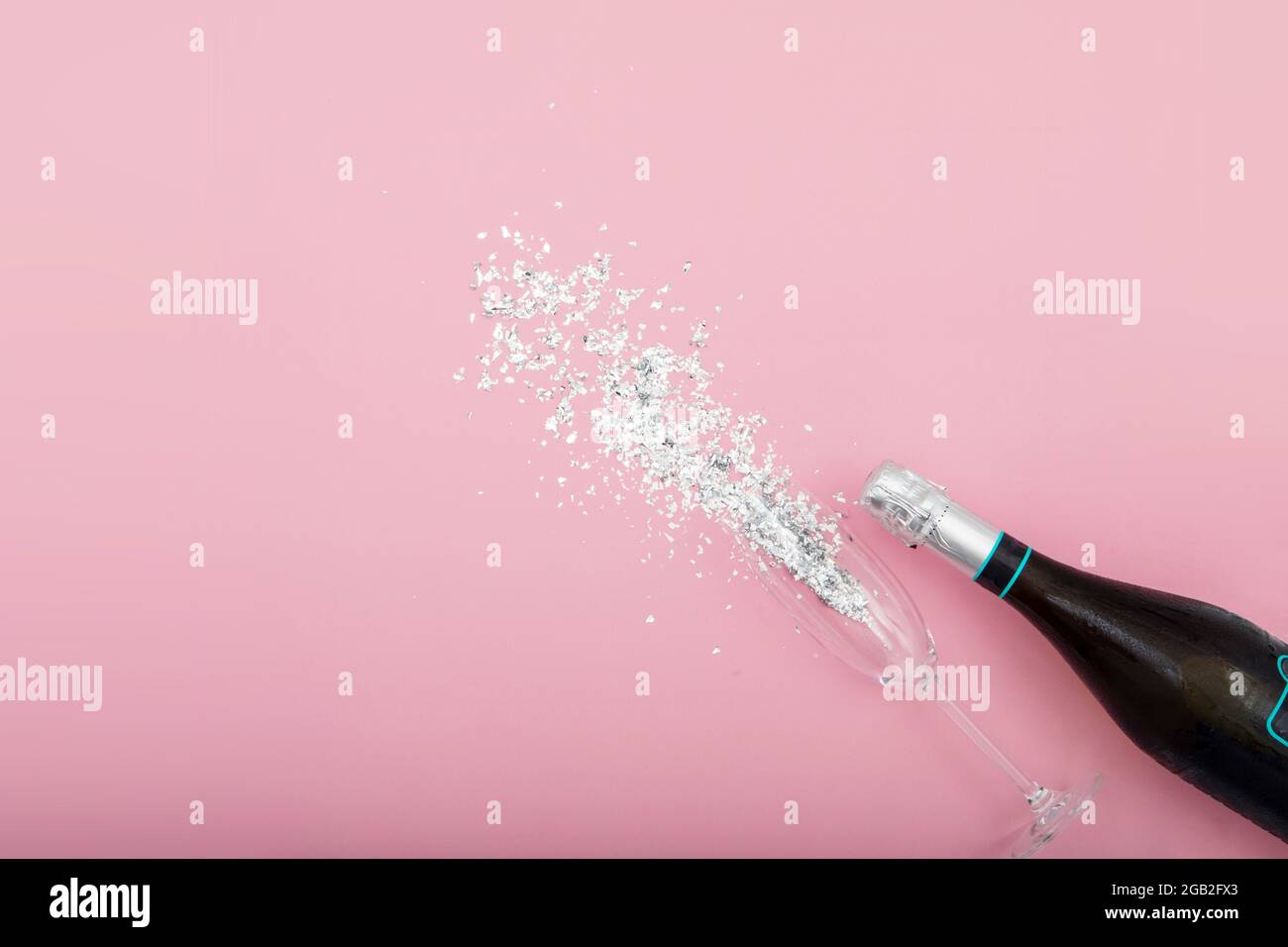 Par-dessus une bouteille de champagne et un gobelet en verre placé sur une table avec paillettes argentées montrant des paillettes sur fond rose Banque D'Images
