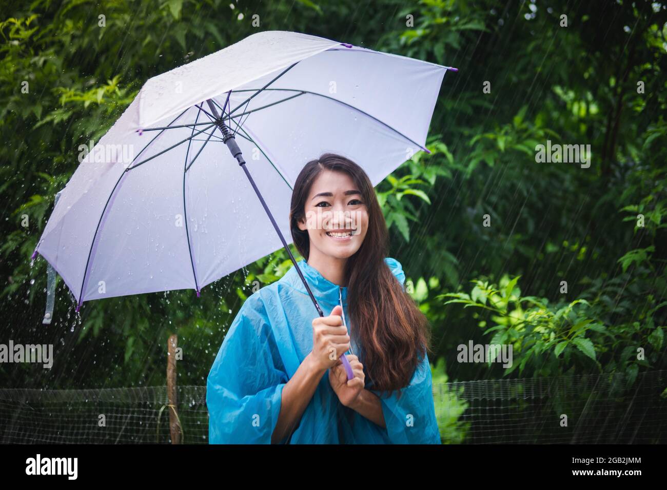 Femme asiatique portant et étendant un parapluie un imperméable à l'extérieur jour de pluie Banque D'Images