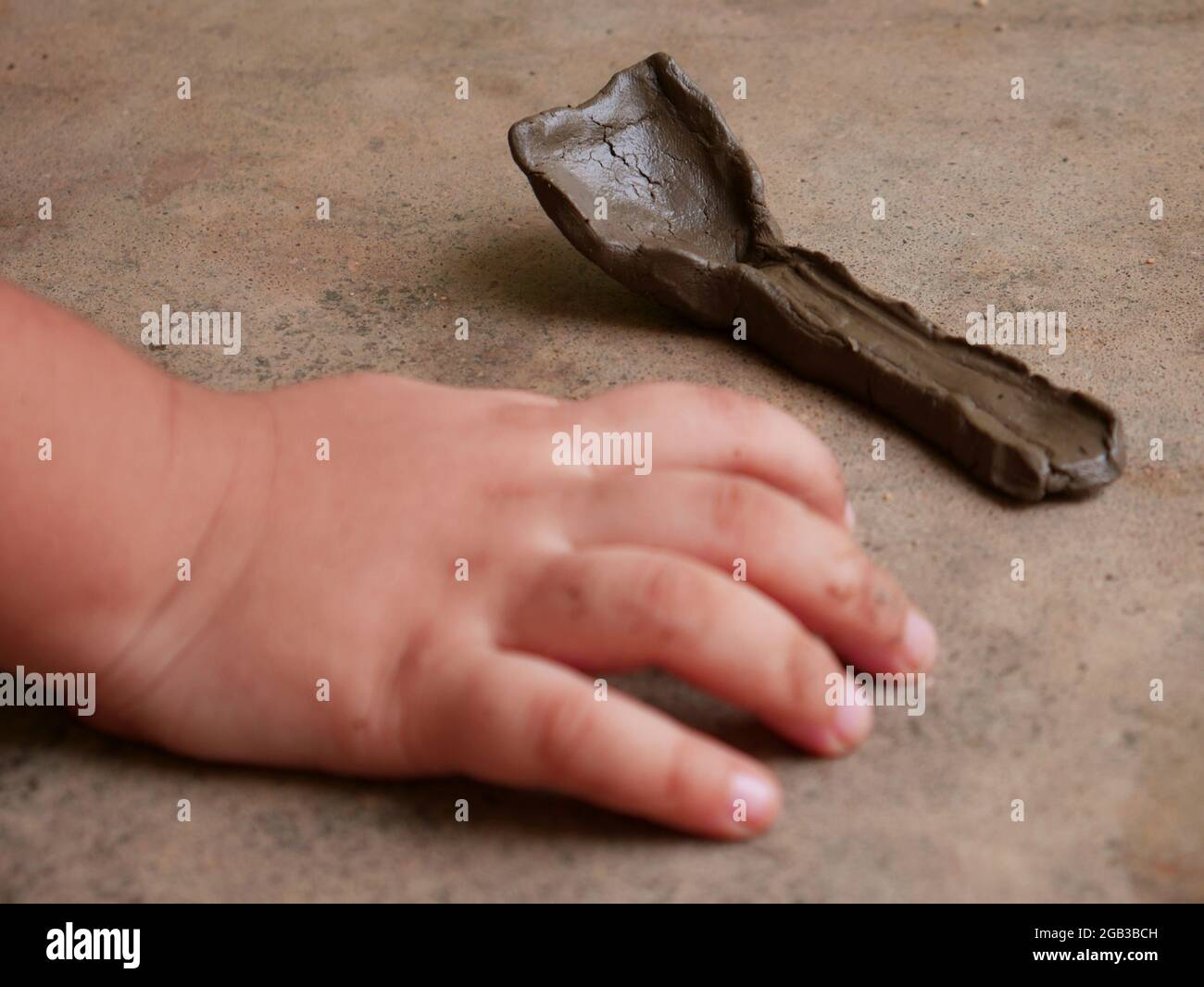 Cuillère faite de terre présentée avec la main d'enfant sur une surface en béton. Banque D'Images