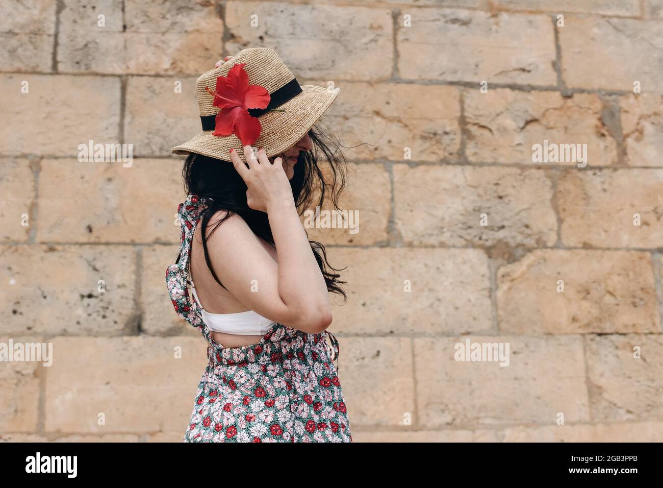 Profil de beau modèle de brunette avec de longs cheveux foncés, chapeau de paille et fleur d'hibiscus. Jeune femme en robe florale d'été. Mode été tendance Banque D'Images