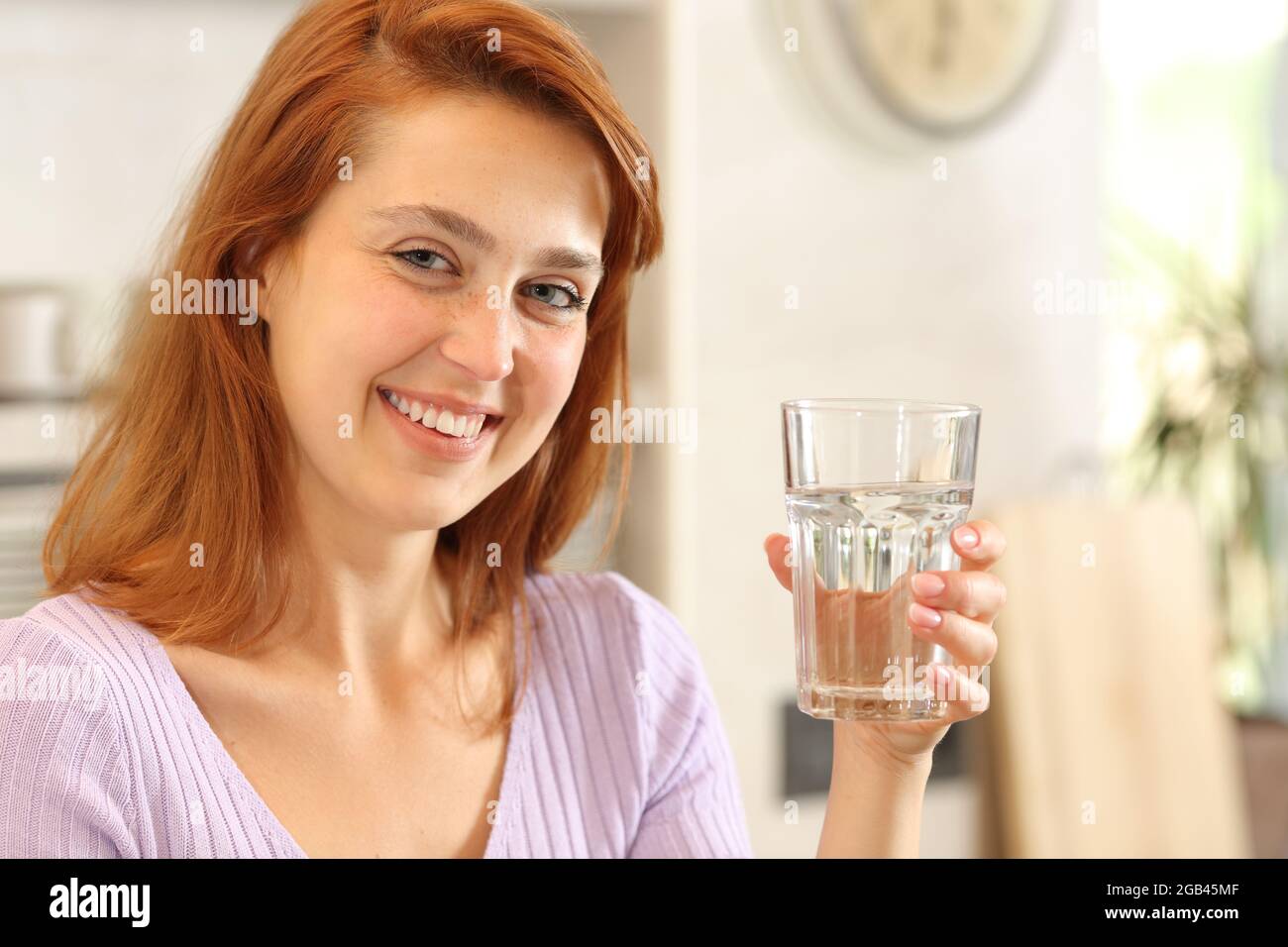 Bonne femme posant regardant la caméra tenant un verre d'eau dans la cuisine Banque D'Images