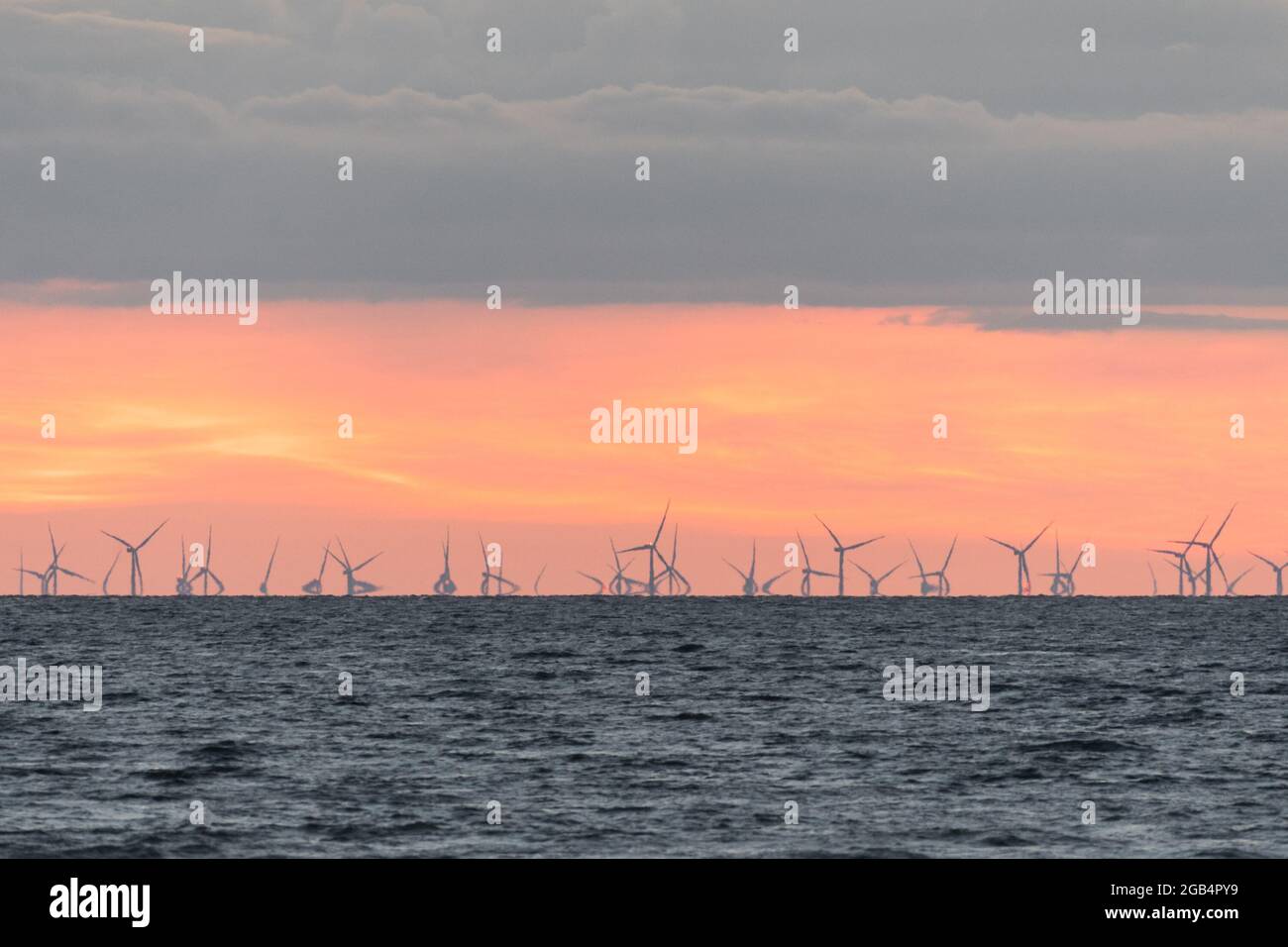 Ferme éolienne dans la mer d'Irlande au crépuscule. Un effet mirage fait que les turbines à l'horizon semblent fléchir lorsqu'elles tournent Banque D'Images