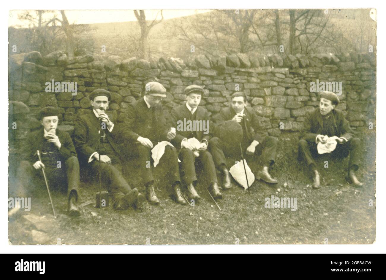 Carte postale originale du début des années 1900 de jeunes hommes qui mangent le déjeuner sur une rampe, vers le début des années 1920 au Royaume-Uni Banque D'Images