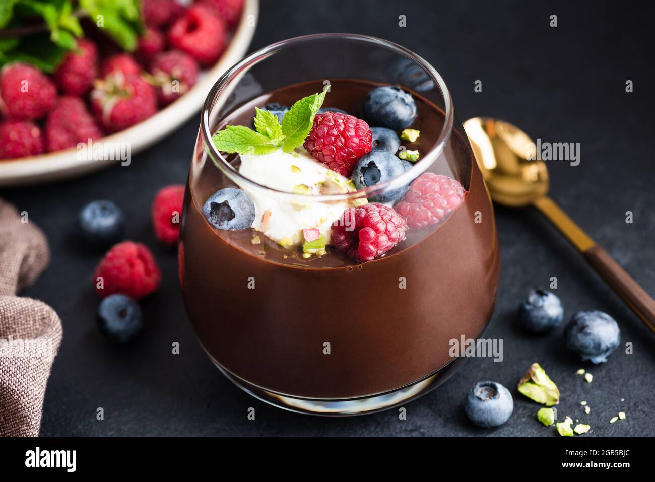 Mousse au chocolat épaisse aux baies de crème et pistaches en verre sur fond de pierre noire. Dessert de luxe mousse au chocolat noir Banque D'Images