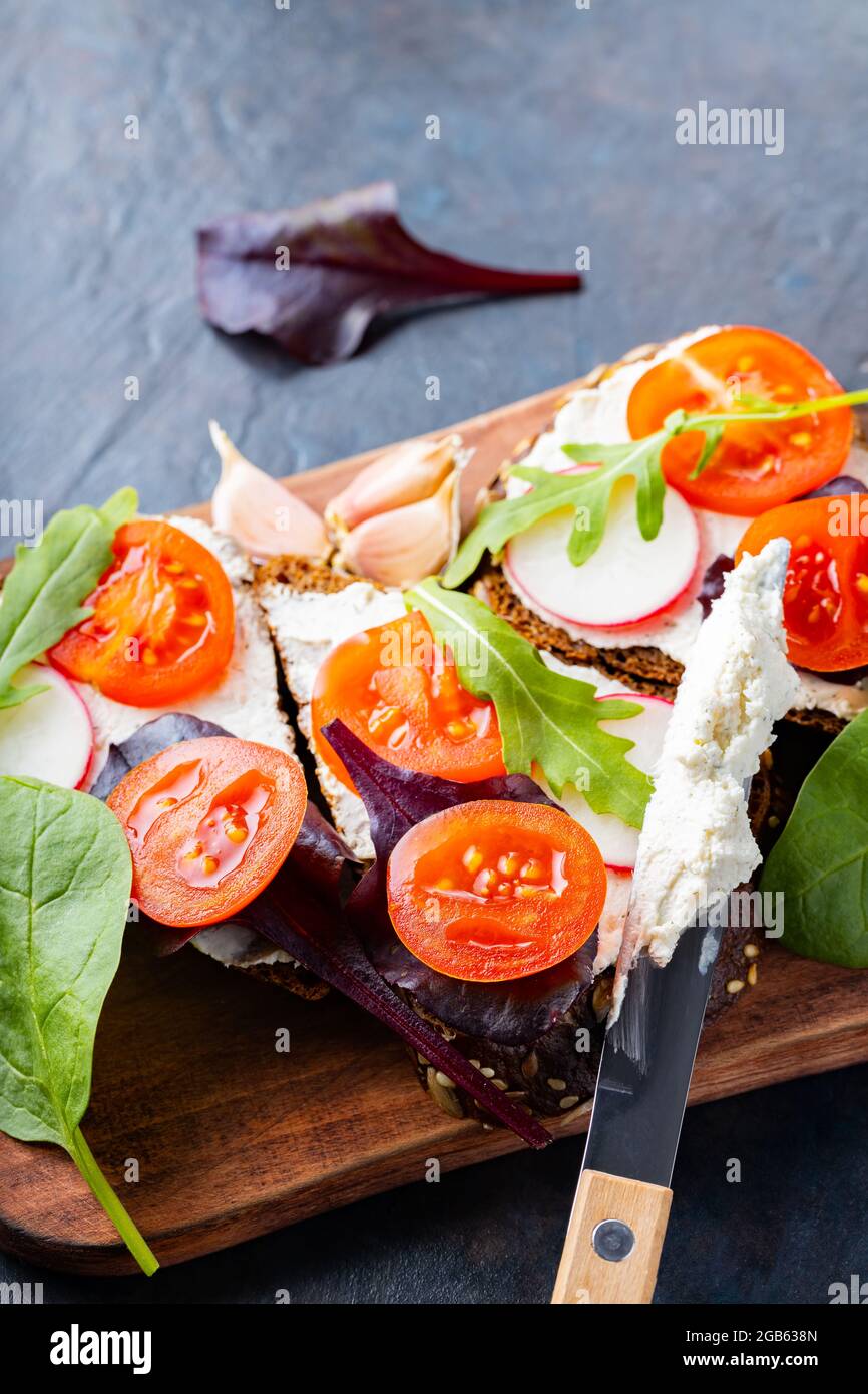 Bruschetta italienne avec fromage à la crème et herbes fraîches. Bruschetta au fromage à la crème, tomates cerises et ail sur une planche à découper. Gros plan Banque D'Images
