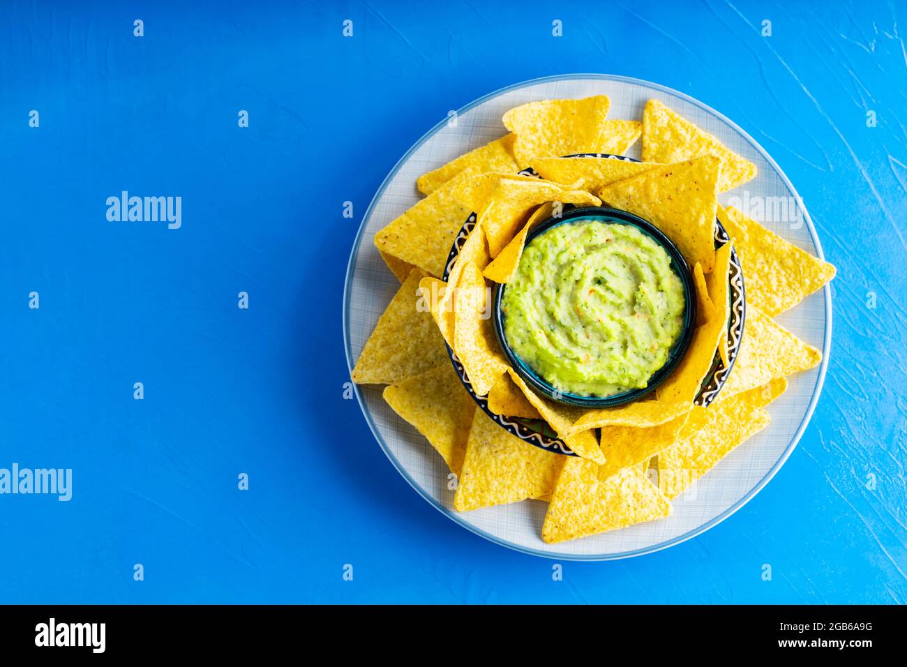 Croustilles tortilla et sauce guacamole sur fond bleu. Guacamole avec copeaux de maïs sur une assiette. Copier l'espace. Vue de dessus Banque D'Images
