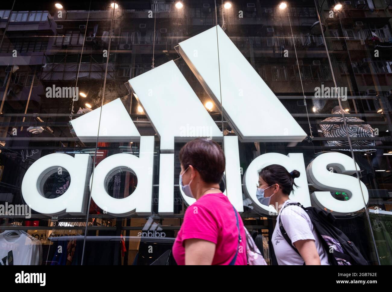 Des piétons marchent devant la marque allemande multinationale de vêtements de sport Adidas magasin et logo à Hong Kong. Banque D'Images