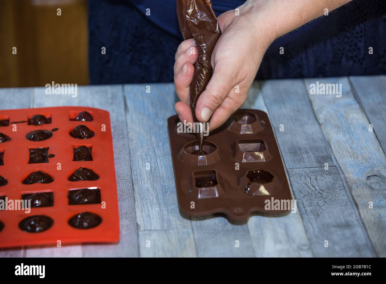 Processus étape par étape de fabrication de chocolats à partir de chocolat noir et de cerises au cognac à la maison. Une femme verse du chocolat chaud dans des moules de bonbons avec prepar Banque D'Images