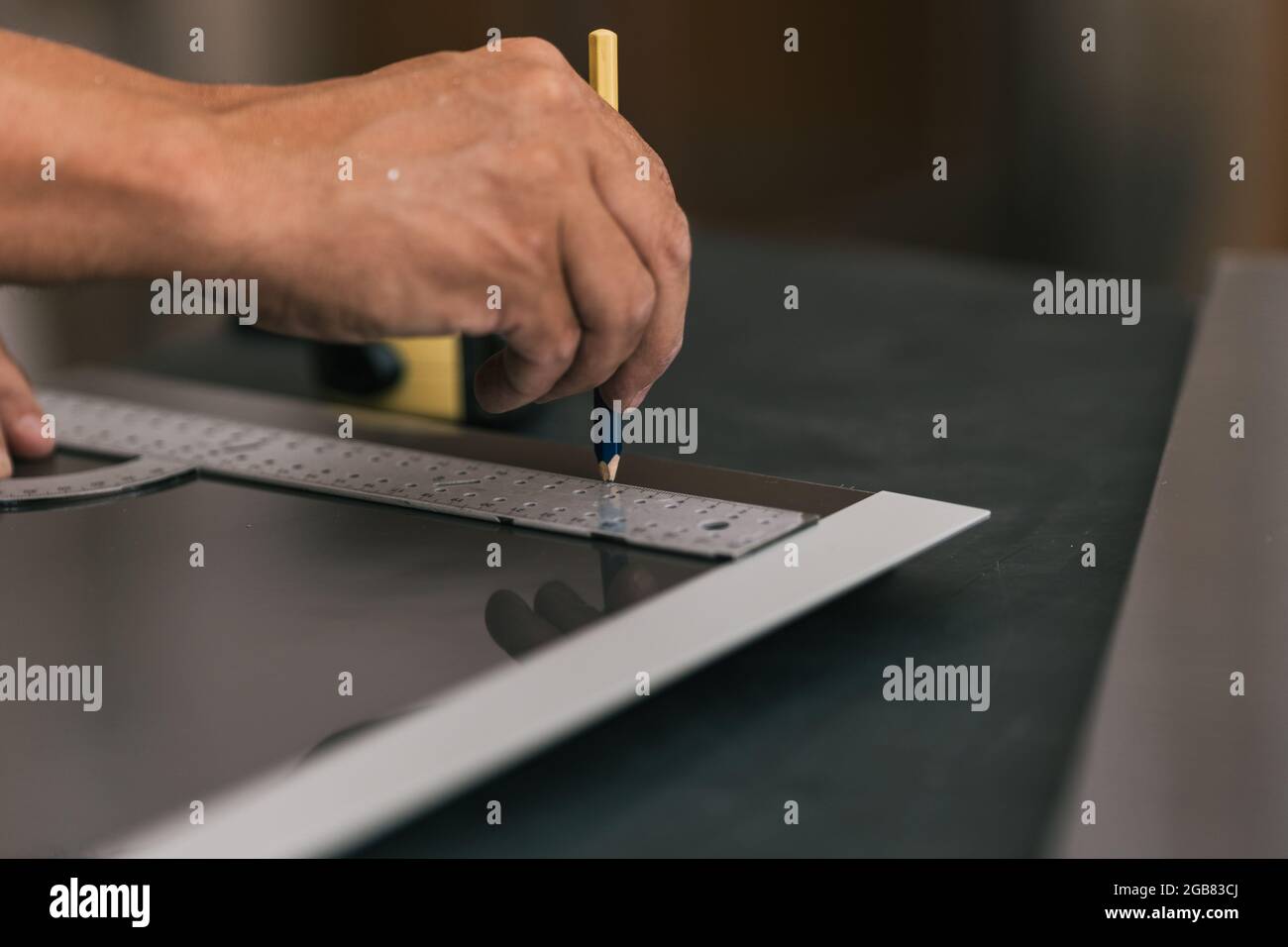 Homme traçant une ligne à l'aide d'un carré sur une surface dans un atelier. Banque D'Images