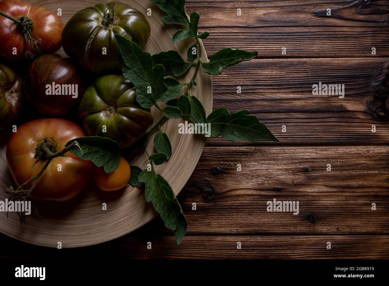 Tomates fraîches dans une assiette en bois sur fond de bois foncé. Récolte de tomates. Touche basse Banque D'Images