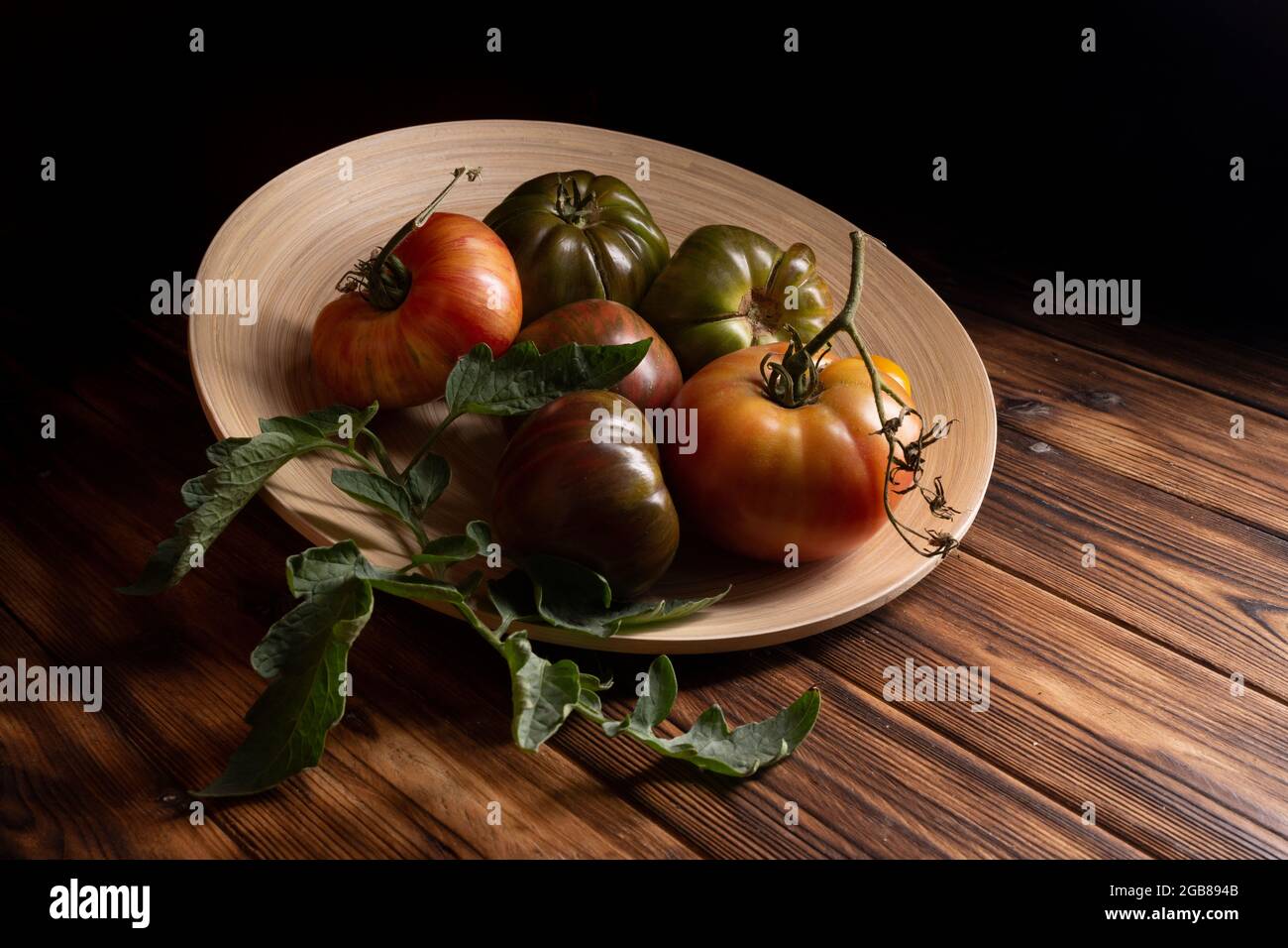 Tomates fraîches dans une assiette en bois sur fond de bois foncé. Récolte de tomates. Touche basse Banque D'Images