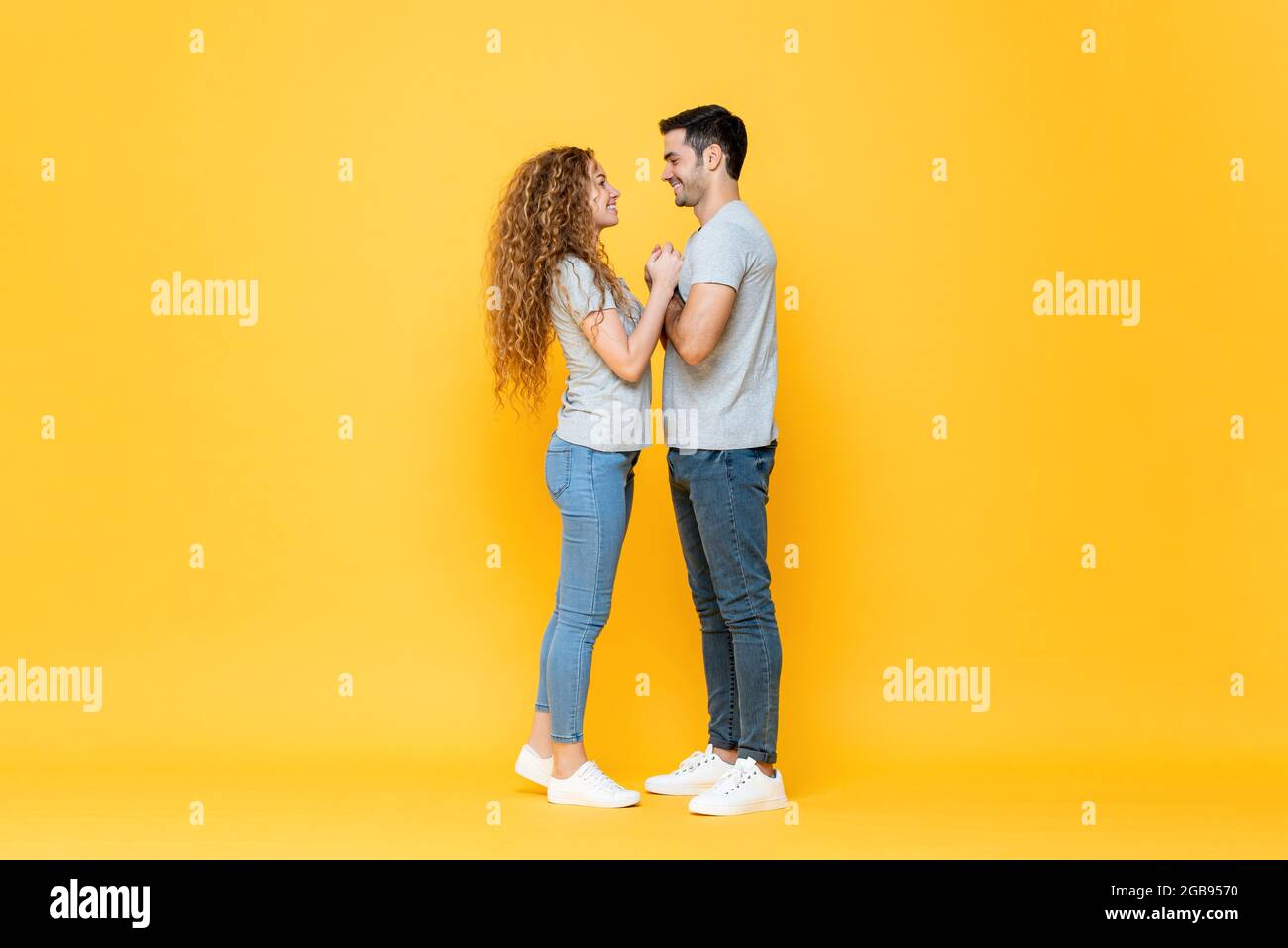 Portrait complet de jeunes heureux couple interracial debout regardant de près dans les yeux et tenant les autres mains dans isolé jaune studio arrière Banque D'Images