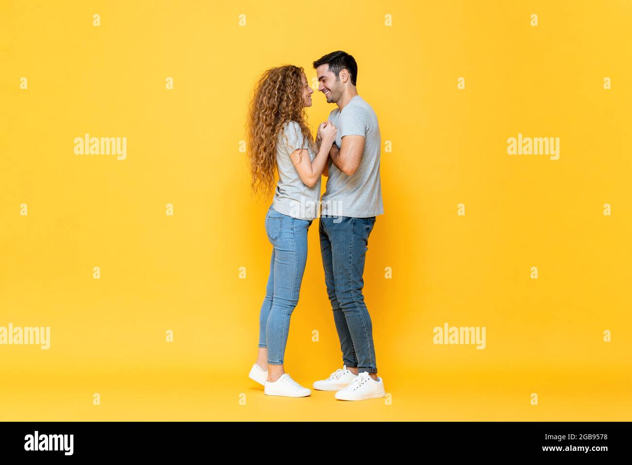Portrait de jeunes heureux couple interracial millénial debout regardant de près dans les yeux et tenant les autres mains dans isolé jaune studio ba Banque D'Images