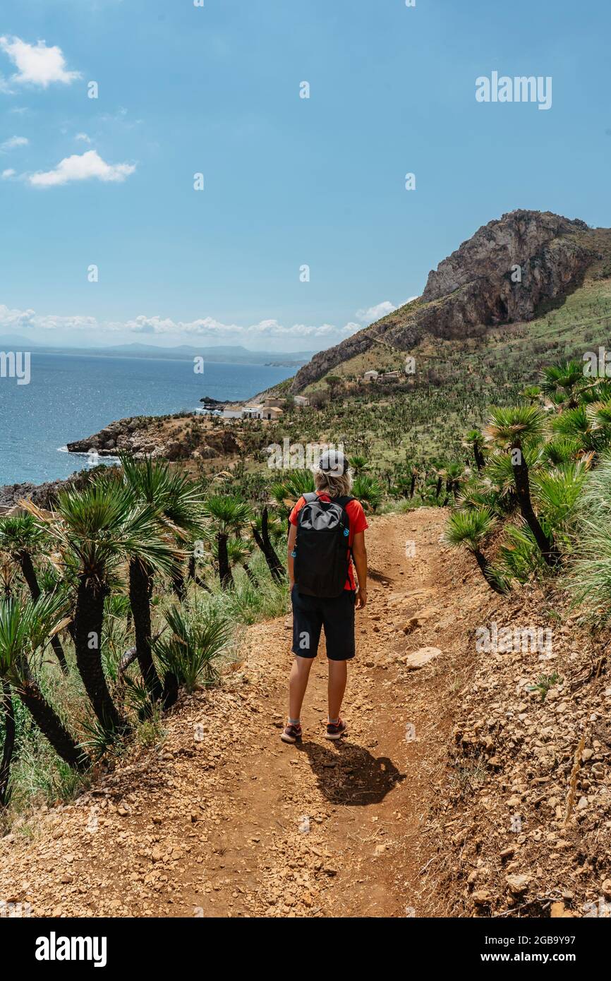 Une femme sportive saine randonnée en Sicile, mer et montagnes en arrière-plan.fille solo avec casquette de baseball appréciant l'escalade et l'aventure d'été. Banque D'Images