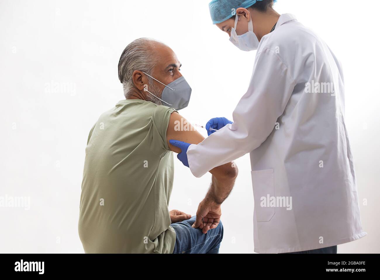 UN VIEIL HOMME PORTANT UN MASQUE FACIAL ÉTANT VACCINÉ PAR UN PROFESSIONNEL DE LA SANTÉ Banque D'Images