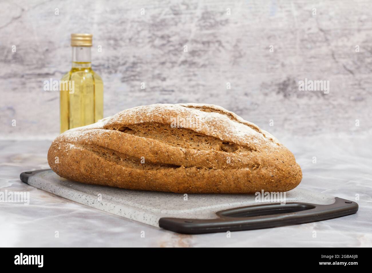 Pain de seigle sur planche à découper et bouteille d'huile de tournesol à fond gris. Banque D'Images