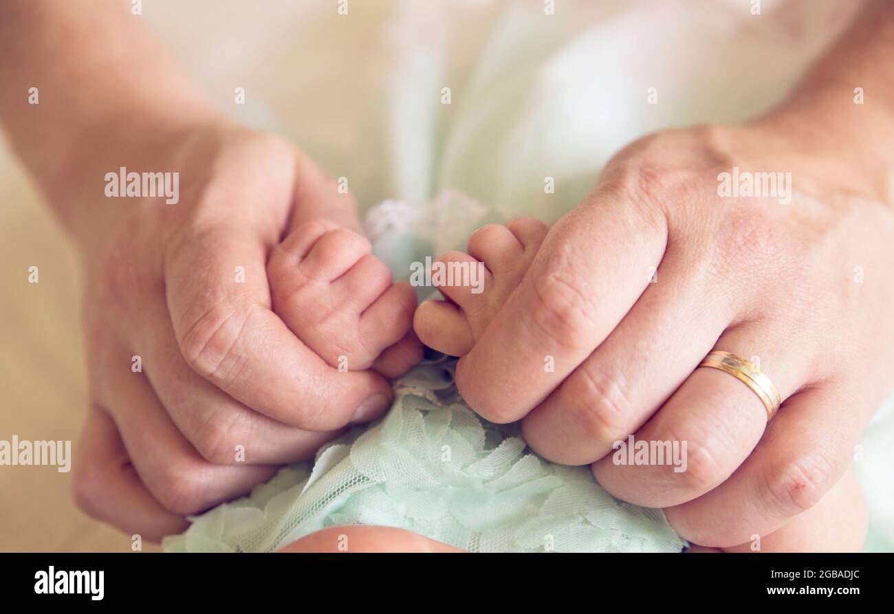 Vue rapprochée des mains du père, doigt avec anneau de mariage, tenant les mains de ses filles nouveau-nées. Concept d'amour. Banque D'Images