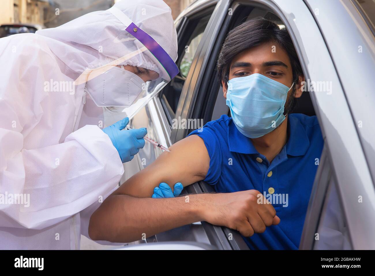 Un travailleur de la santé en kit d'EPI vaccinant un homme en voiture avec le vaccin corona. Banque D'Images