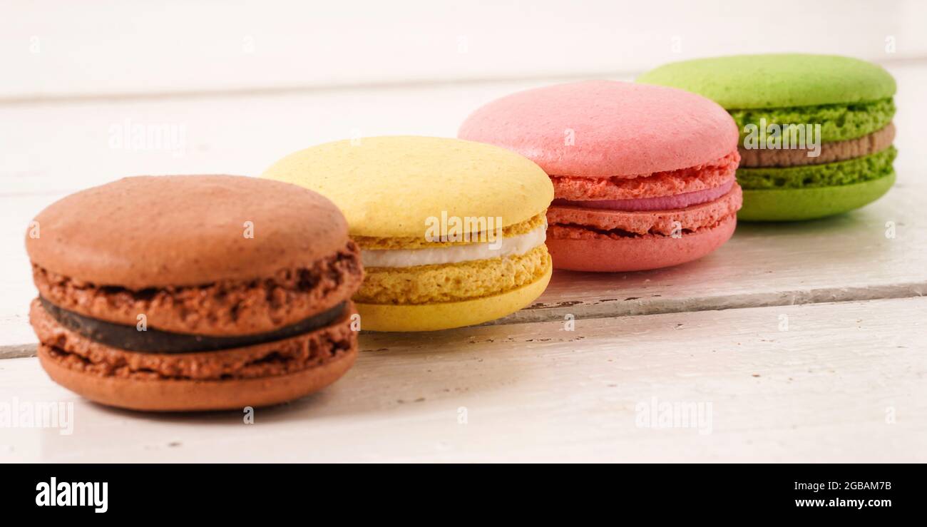 Bannière. Quatre macarons colorés verts, roses, jaunes et bruns sur fond rustique en bois blanc. Macarons de petits gâteaux français doux et colorés. Banque D'Images