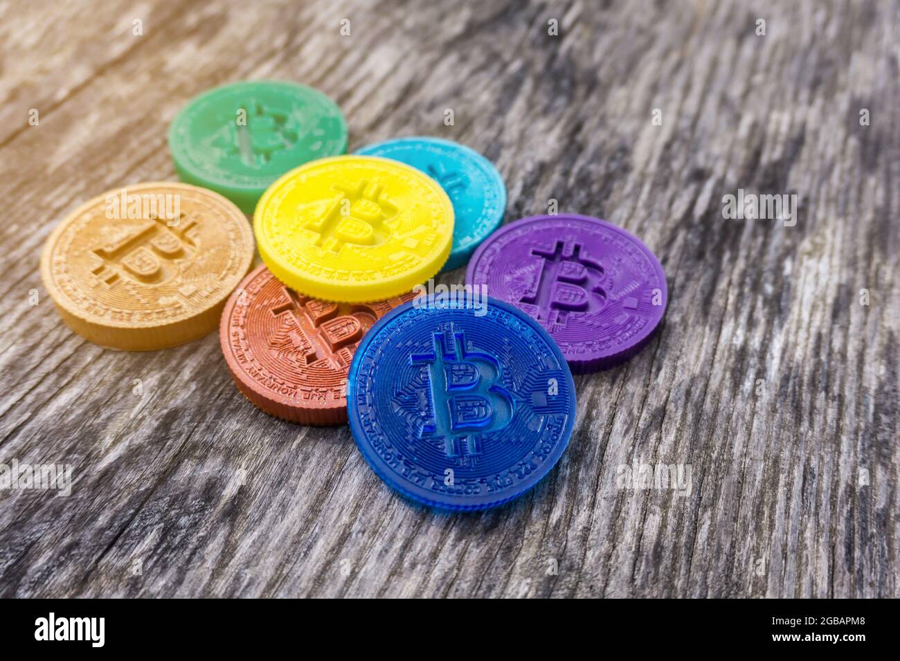 Pièces de monnaie en bitcoin dans les couleurs arc-en-ciel sur fond en bois. Crypto-monnaie multicolore fait main. Sept pièces différentes en rouge, orange, jaune, vert, Banque D'Images