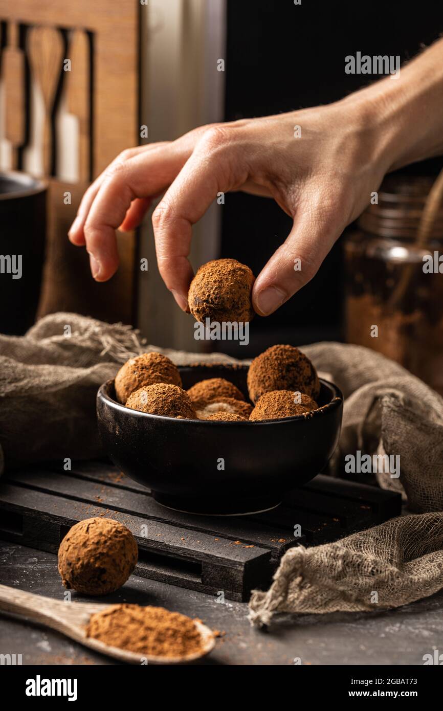 Femme à la main de prendre une paix de délicieux boule de cacao maison avec des ingrédients sains d'une assiette noire, recouverte de poudre de cacao Banque D'Images