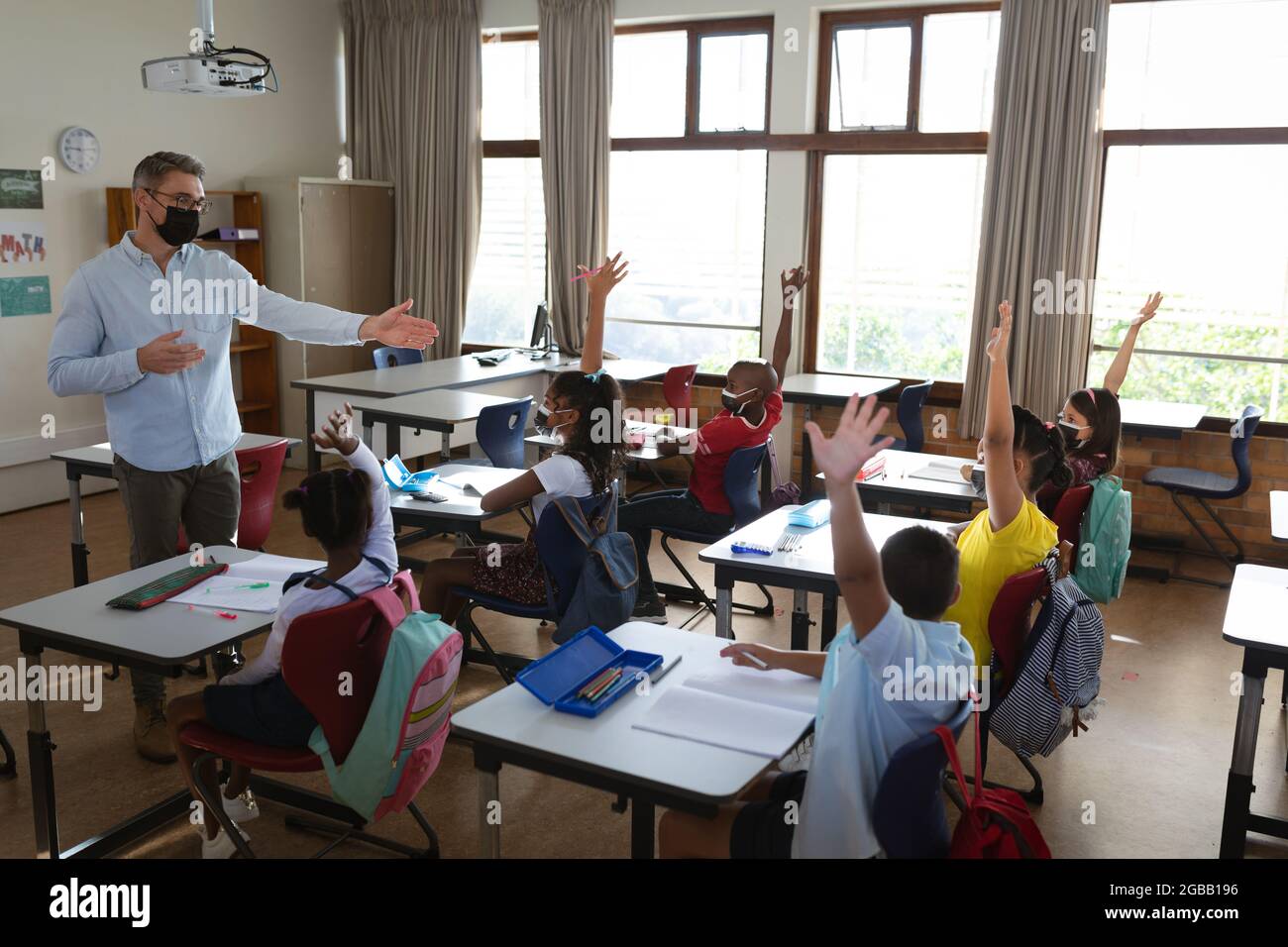 Groupe d'élèves divers portant un masque facial levant les mains dans la classe à l'école Banque D'Images