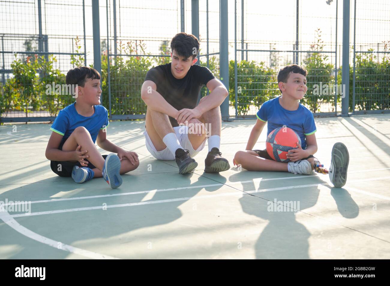 Un entraîneur assis sur le terrain de football et parlant avec deux étudiants. Banque D'Images